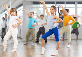 Positive juvenile girl engaged in Rock-n-Roll dance together with children's group and female trainer in training room