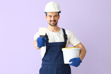 Male decorator with putty knife and bucket on lilac background
