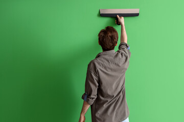 Young man with putty knife on green background, back view