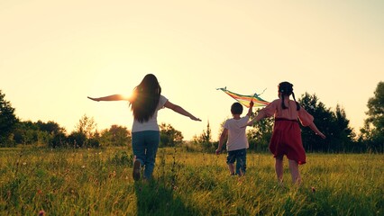 Mom Boy, girl play with toy kite in park in spring. Children toy plane. Kite flies in hands of...