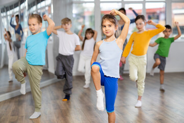 Dynamic little girl training hip hop dance poses with instructor and other attendees of dancing...