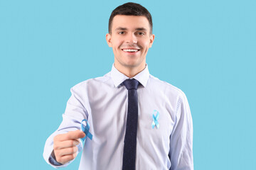 Young businessman with blue ribbons on color background. Prostate cancer awareness concept