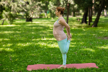 Fototapeta premium Pregnant caucasian woman doing yoga in the park. Balance on one leg.