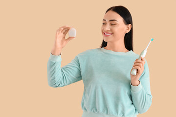 Beautiful young happy woman with dental floss and electric toothbrush on beige background