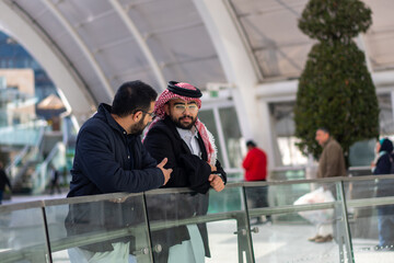 Two arabic males are talking to each other in modern place outdoors like mall shop and huge playing...