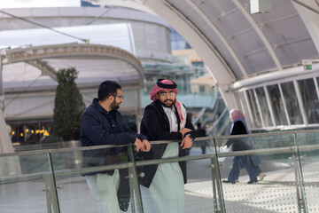 Two arabic males are talking to each other in modern place outdoors like mall shop and huge playing areas about there work life and problems