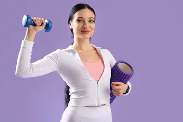  Portrait of sporty young woman with dumbbell and body roller on lilac background © Pixel-Shot