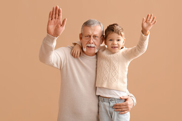 Grandfather with his happy cute little grandson waving hands on beige background