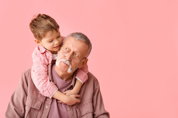Grandfather with his happy cute little grandson hugging on pink background