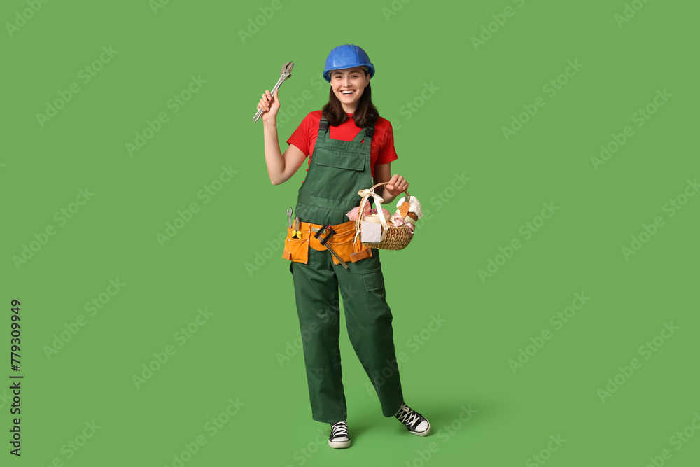 Poster Happy female builder with Easter basket, adjustable wrench and tools on green background