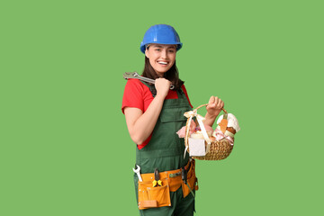 Happy female builder with Easter basket, adjustable wrench and tools on green background