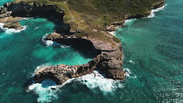 Aerial view of vibrant ocean waters create swirling patterns along rocky, picturesque coastline of tropical island. Waves crash against rocks in turquoise Caribbean Sea near Macao, Dominican Republic.