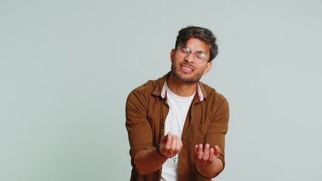 Give me money, please. Indian man rubbing fingers show cash gesture, demands to pay back the debt, take loan, do shopping, begging, investment, reward. Arabian guy isolated on studio gray background