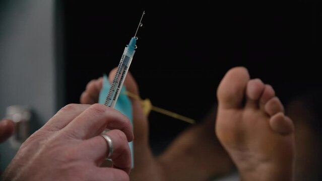 Hand holding syringe in front of a morgue body