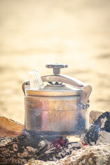 A closed pressure cooker with a water glass on the valve. Cooking over a wood and charcoal fire...