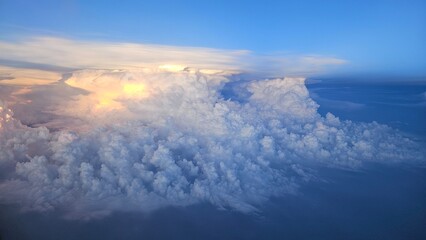 Flying above the blue sky clouds on sunset of airplane flight. View from the window of the plane in...