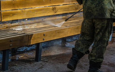 A worker washes park benches with pressurized water.