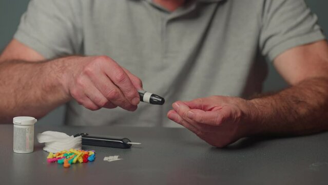 An elderly man diagnosed with diabetes takes a quick blood sugar test using a portable glucometer with replaceable needles. Closeup
