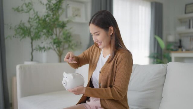 Young Asian woman putting coin in piggy bank. Save money and financial investment