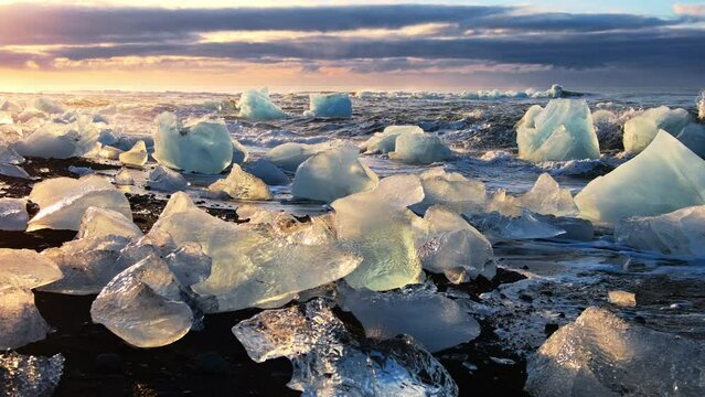 Icebergs Shining During Golden Hour, Sunrise on Diamond Beach in Iceland. Clear Ice Crashed by Ocean Waves. Black Volcanic Beach. Climate Change and Global Warming Problem. Epic Winter Nature.