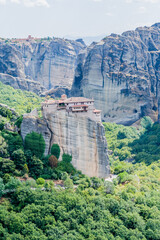 Secluded cliffside monastery with striking greenery at the base of towering rock formations in Meteora, Greece