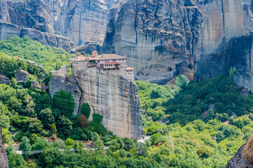 Secluded cliffside monastery with striking greenery at the base of towering rock formations in Meteora, Greece