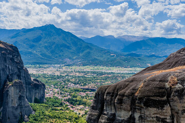 Panoramic view of a lush valley surrounded by mountains and rock formations in Meteora, Greece.