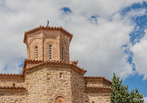 Stone church with a prominent bell tower against a cloudy sky in Meteora, Greece.