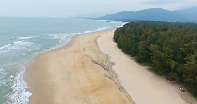 Beautiful Shimei Bay beach scenery of Wanning Hainan China, Waves crashing on the white sandy clean beach with Dense woods and distant green mountains in the fog