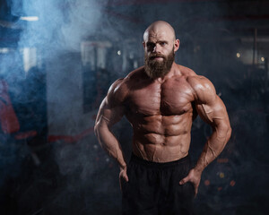 Fototapeta na wymiar Muscular bald man posing shirtless. Bodybuilder showing off his shape in the gym. 