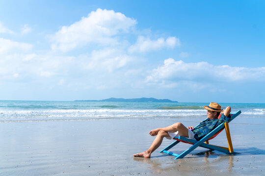 Happy Asian man relax and enjoy outdoor lifestyle travel ocean on summer holiday vacation. Handsome guy relaxing and sleeping on sunbed at tropical island beach in sunny day. People and nature concept
