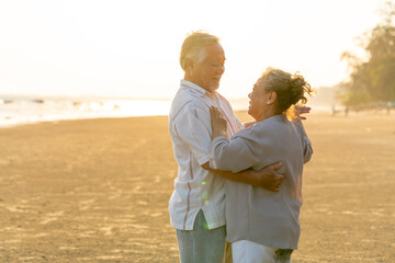 Happy family Asian senior couple having romantic moments dancing together at tropical beach at summer sunset. Elderly husband and wife enjoy outdoor lifestyle travel nature ocean on holiday vacation.
