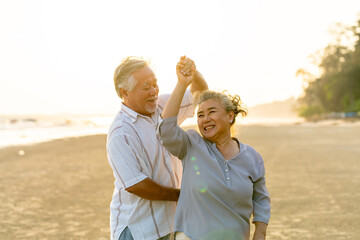 Happy family Asian senior couple having romantic moments dancing together at tropical beach at summer sunset. Elderly husband and wife enjoy outdoor lifestyle travel nature ocean on holiday vacation.