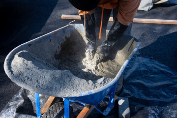 Closeup of a construction worker with black rubber gloves mixing up cement by hand in a wheelbarrow
