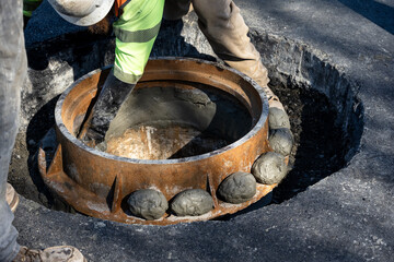 Closeup of a construction worker with black rubber gloves using wet cement to seal a sewar access point collar to the pipe below, road construction project
