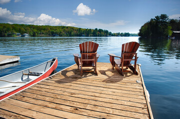 Tranquil Muskoka, Ontario setting as two Adirondack chairs grace a wooden dock by the shimmering...