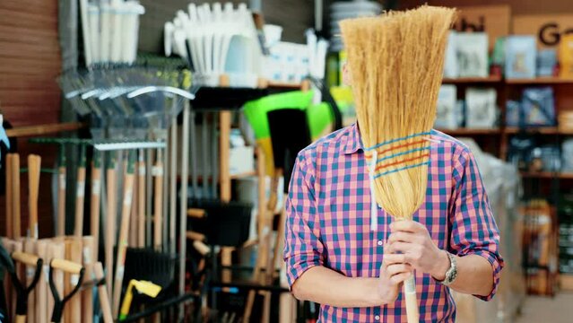 Male buyer carefully chooses broom in hardware store to clean the yard of her house. High quality 4k footage