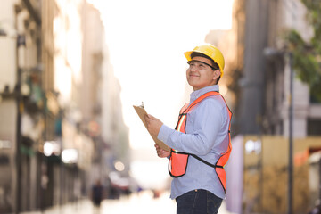 Mexican working man with hard hat and goggles looking at the horizon smiling against an urban...