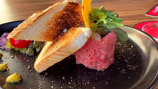 Tasty beef steak tartare with toast bread and a pickle on a plate, raw meat dish, 4K shot