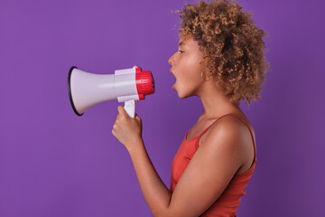 Young curly excited African American woman promoter holds white megaphone and loudly announces...