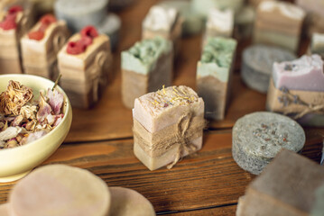 A lot of pieces of fragrant, beautiful natural soap on a wooden table in the workshop and the hand of a woman soap maker carefully takes one piece