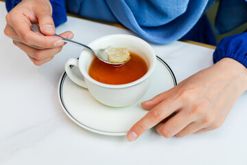 Closeup of woman putting rock candies into the cup of black tea