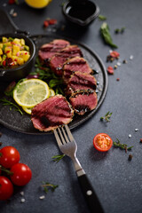 Sliced Organic grilled Tuna fillet covered with sesame seeds and mango salsa on black ceramic serving board