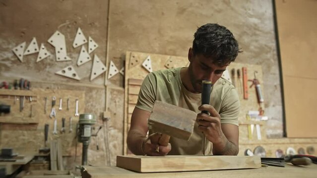 Young man carpenter carving wood block. Guy process timber bar. Male carpentry work skill. Joiner woodwork. Worker beat hammer. Person use chisel. Diy master class workshop Woodworker make job project