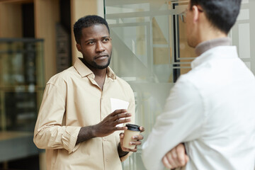 Waist up portrait of confident Black young man chatting with colleague during coffee break in...