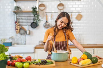 Young woman standing near stove and cooking, housewife, meal, chef, food.Happy woman looking and smelling tasting fresh delicious from soup in a pot with steam at white interior kitchen