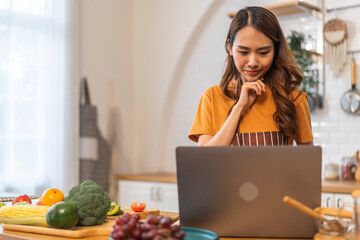Asian young woman holds a wooden spoon with online audience or simply enjoying the cooking process, health, fruit, freshness, and organic living, digital recipe platform, eating, healthy at kitchen
