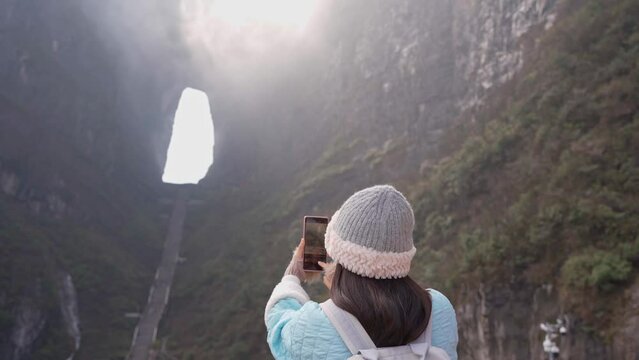 Young female tourist taking a photo of the The Heaven's Gate at Tianmen Shan national park, The famous tourist destination at Zhangjiajie