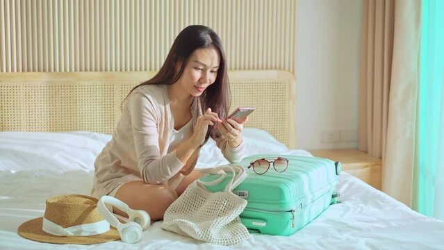 Happy young Asian woman packing her luggage and planning a summer vacation trip, Travel concept