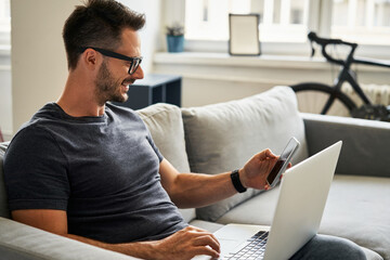 Man sitting on sofa doing online payments with laptop and phone